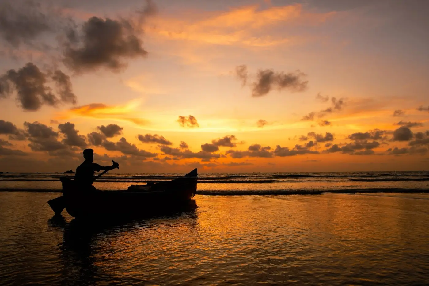 A fisherman paddling a canoe off Muzhappilangad beach at sunset
