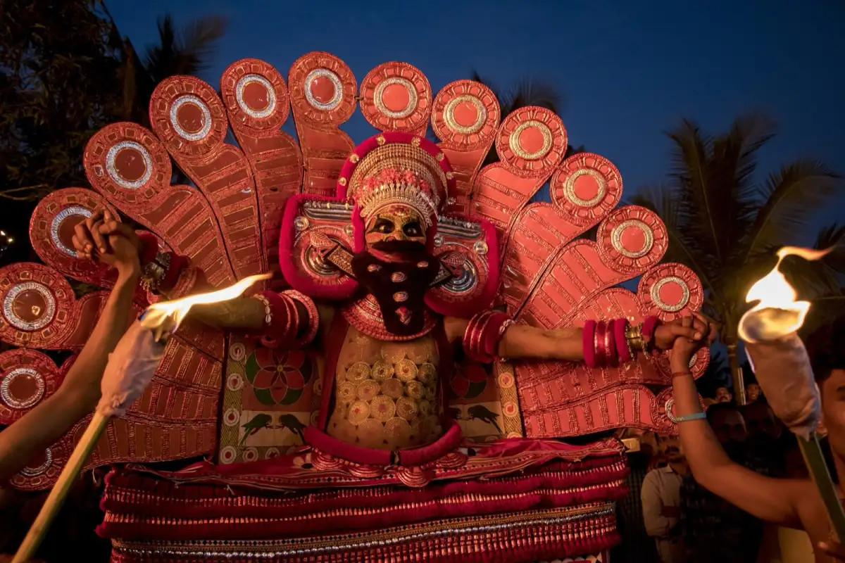 A Theyyam performer with torchbearers at dusk